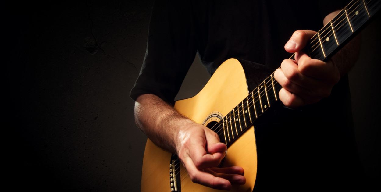 Mężczyzna trzymający gitarę akustyczną. Zdjęcie ilustracyjne. Depositphotos